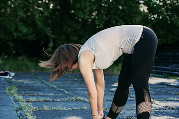 An adult woman is doing fitness in the park. The woman is bending forward.