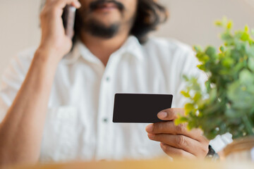 Selective focus of adult bearded man holding credit card and talking on cellphone.