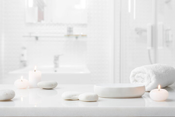 Marble table for spa product display with stones, burning candles and towel on blurred bathroom...