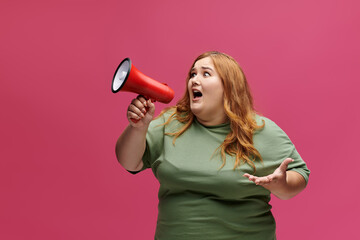 A woman with long red hair and a green shirt holds a megaphone and shouts.