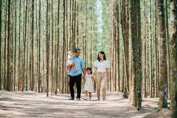 Fototapeta premium A happy Asian family walking through a park in the spring, with their baby in a stroller and their daughter holding their hands, Happy family day