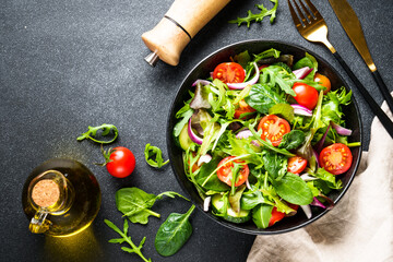 Green Salad with salad leaves and vegetables at black background. Top view with copy space.