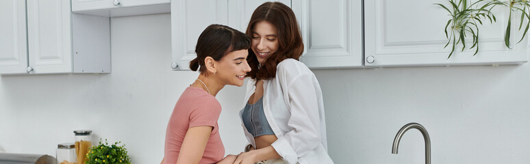 A young lesbian couple shares a tender embrace in their kitchen, their love and connection evident in their morning glow.