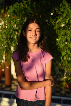 11-year-old girl entering puberty pictured in the courtyard of her house, looking at the camera happily with a jasmine in the background