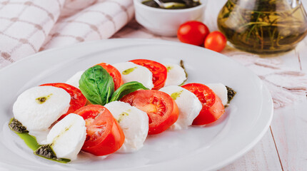Caprese salad with tomatoes, mozzarella cheese, pesto and basil on white plate