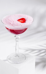 Pink cocktail standing on white cube with strawberry garnish