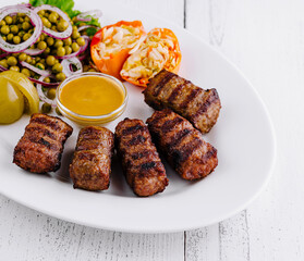 Grilled minced meat kebab with mustard, pickles, and green pea salad on white plate
