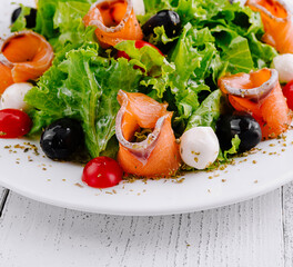 Fresh salad with lettuce, tomatoes, mozzarella, olives and salmon on white plate