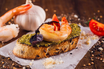 Delicious bruschetta with pesto sauce and grilled shrimps on wooden table