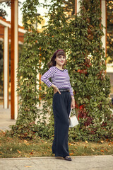 A young woman fashionably dressed in a vintage straw hat walks in an autumn park.