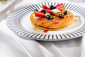 Delicious pancakes lying on a plate with strawberries, blueberries, pistachios and syrup