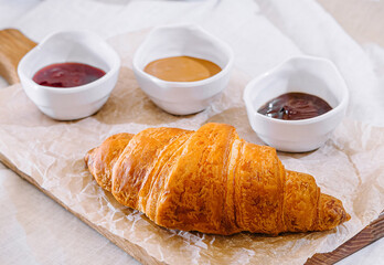 Freshly baked croissant with bowls of jam and peanut butter for breakfast