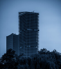 Fototapeta premium Urban Skyscraper Under Construction Surrounded by Lush Greenery