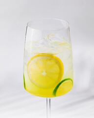 Glass of refreshing lemonade with lemon and lime slices on white background