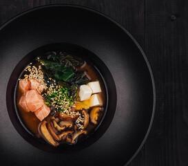 Steaming miso soup with salmon and shiitake mushrooms in black bowl