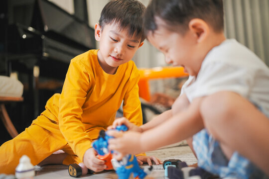Two asian young boys play with action figures on the floor, enjoying a fun and imaginative playtime in a cozy home environment.