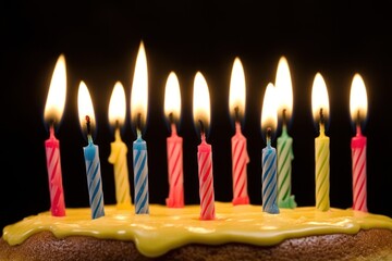 Birthday cake with colourful candles lit on a dark background.