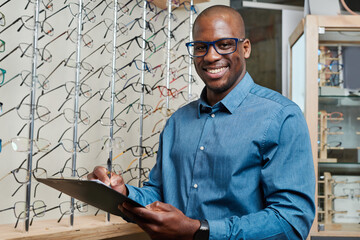 Optometrist Business Owner Smiling Confidently with Clipboard in Eyeglass Store