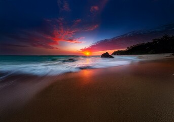 A vibrant sunrise illuminates a serene beach with smooth waves gently crashing on the shore.