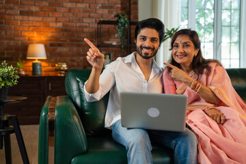 Elderly Indian woman and young son using laptop for online shopping in a cozy living room