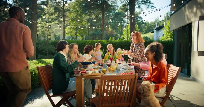 Diverse Group of Friends Enjoys an Outdoor Barbecue, Dining and Toasting in a Beautiful Garden Setting. Man Grills Food while Others Sit at a Wooden Table, Sharing Laughter and Conversation