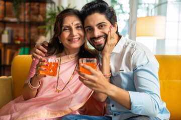 Elderly Indian mother and son share orange juice and laughter while sitting on a sofa