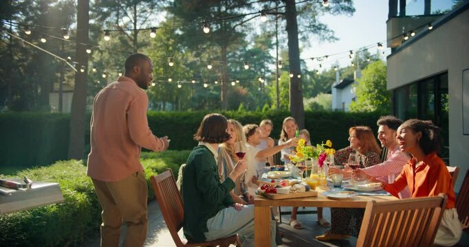 Group of Friends Having an Open Air Barbecue Dinner in Their Backyard. Old and Young People Talk, Chat, Have Fun, Eat and Drink. Hosts are Bringing Food From the Grill to the Table