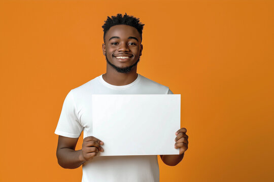 A young African-American man with a smile on his face in a white T-shirt and holding a white sign in his hands, on an orange background. Advertising banner.