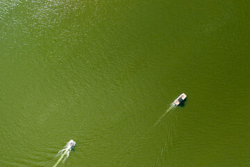 Aerial view of boats gliding on a greenish lake, showcasing serene water patterns. Ideal for nature and travel themes.