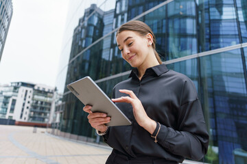 Young Professional Woman Using a Tablet While Standing Outside Modern Office Buildings in an Urban Setting During the Day