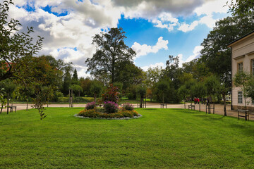 Fototapeta premium Gepflegte Parkanlage von Schloss Pillnitz mit zentralem Blumenbeet und altem Baumbestand unter sommerlichem Wolkenhimmel, Dresden, Sachsen, Deutschland