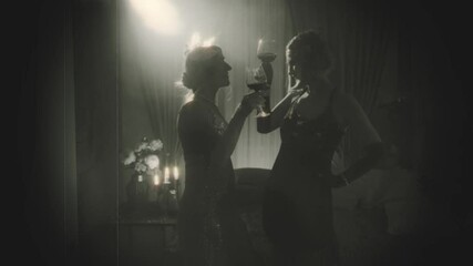 Old film 1920s style black white color. Dark silhouette two happy women clink glasses drinking red wine, dark room night club full smoke. Retro lady Woman in evening dress. Sexy girls new year party