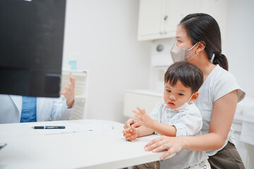 Fototapeta premium Mother with son at a doctor's office, both wearing masks for safety during a consultation, emphasizing health and protection.