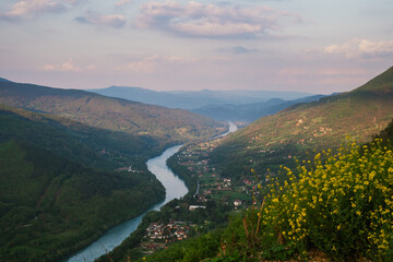 Scenic view of a winding river flowing through lush hills and valleys under a soft evening sky