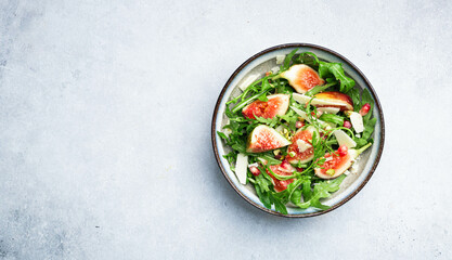 Salad with arugula, figs, cheese and pomegranate, healthy food. Top view, copy space