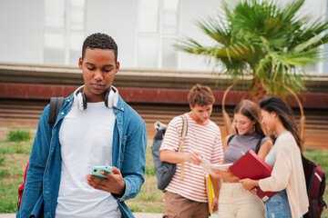 Serious african american teenage student using a cellphone at university campus. Isolated guy watching bad news on his smartphone on the high school. Young man standing with a mobile phone outside