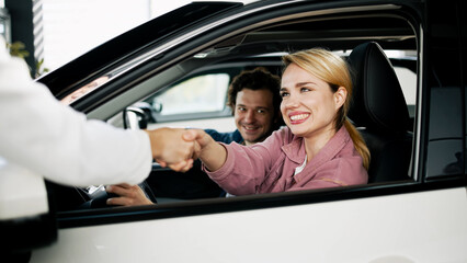 A family couple celebrates their decision to buy a sleek new car at the dealership. Their genuine smiles capture the joy of making an important investment in their family's future and adventures.