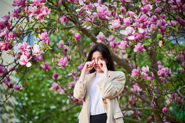 Woman allergic suffering from seasonal allergy at spring in blossoming garden at springtime. Young...
