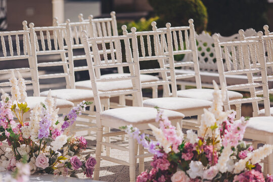 Ceremony in the bosom of nature. White chairs with flowers set in the grass. white chairs lined up for an event accompanied by a bouquet of white flowers. 
