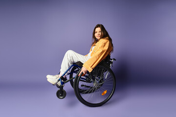 A young woman in casual clothing sits in a wheelchair against a purple backdrop.