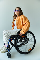 Brunette woman in wheelchair wears casual attire, sunglasses, gazes confidently to the side against...