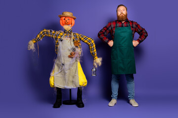 Photo of confident man farmer with scarecrow doll guarding field halloween autumn time isolated on purple color background