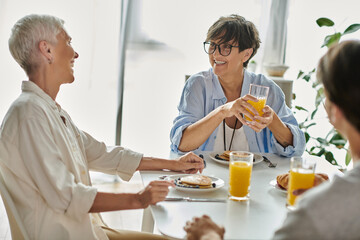 A cozy morning as lesbian parents enjoy breakfast with their adult son, filled with laughter and connection.