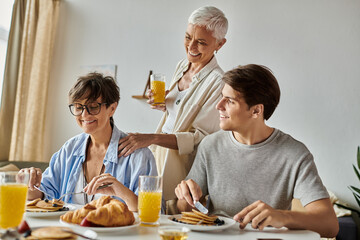 A joyful moment as a lesbian couple shares breakfast with their adult son, surrounded by warmth and love.
