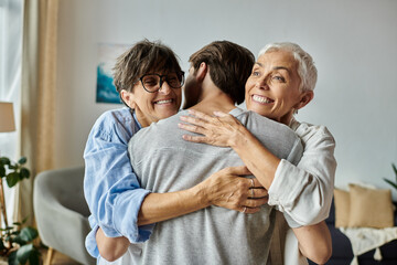 Fototapeta premium Lesbian parents and their adult son share warm hugs and laughter in their cozy living room.