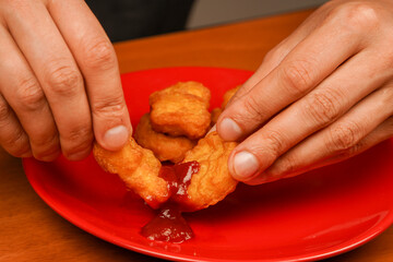 Holding chicken nuggets. Man eating chicken nuggets. Chicken nuggets with ketchup. Fast food. Junk food. Unhealthy lifestyle. Calories. Obesity. American food.