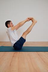 Focused Latin athlete performs morning exercise at home, holding the boat pose on a yoga mat. He...