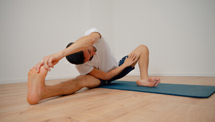 Fototapeta premium White Latino male performing the open pincer pose (Prasarita Padottanasana) during a yoga session at home, demonstrating strength and balance.