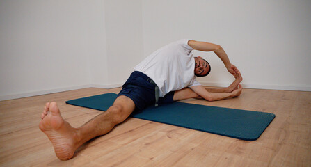 Naklejka premium White Latino male performing the open pincer pose (Prasarita Padottanasana) during a yoga session at home, demonstrating strength and balance.