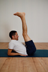 Fototapeta premium Athletic Latin man performs an advanced boat pose variation at home on a yoga mat. He balances while strengthening his core and flexing abs, showcasing concentration and body control